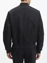 Campera bomber negra Calvin Klein de satén de nailon reciclado, con cuello, puños y bajo de punto de canalé. Tiene cierre de cremallera, bolsillos de hendidura en la cintura, detalle de cremallera en la manga e insignia con el logo de goma de Calvin Klein en la manga. El forro y el relleno son de poliéster reciclado REPREVE®.