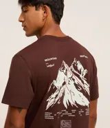 Remera marrón de algodón, corte clásico, con cuello redondo y manga corta. Presenta un pequeño estampado con lettering y un logo en el pecho.