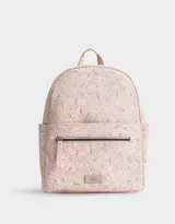 Mochila rosa claro de cuerina estampada con flores blancas. Tiene correas regulables, manija superior, acceso con cierre, bolsillo frontal con cierre y tag de cuerina.