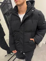 Campera puffer negra de nylon impermeable con capucha forrada en corderito desmontable, cierre frontal con botones a presión y bolsillos laterales.