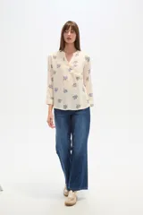 Blusa de manga tres cuartos color crema con estampado floral en azul. Presenta cuello mao con abertura en V y un bolsillo de parche en el pecho.