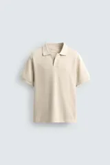 Polo color beige de punto con textura acanalada, corte relaxed, cuello solapa con abertura frontal y manga corta.