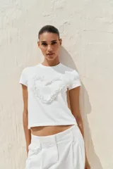 Camiseta blanca de algodón con cuello redondo, manga corta y detalle de corazón con tejido en relieve en el delantero.