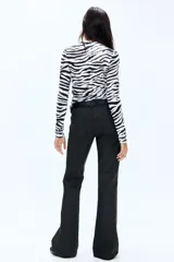 Jean de cinco bolsillos color negro, con tiro bajo y cierre de botón. Presenta un corte ajustado en la parte superior y piernas acampanadas.