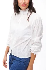 Camisa blanca de algodón con cuello alto con volados, mangas largas abullonadas y cierre frontal con botones.