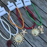 Collar de cordón trenzado en colores naranja, blanco y verde, con dijes colgantes de estrella de mar dorada, caracol rojo y langosta dorada.