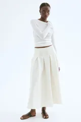 Pollera midi color crema, de tiro alto, con tablas y silueta evasé.