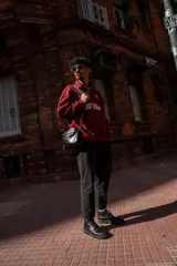 Bandolera negra de cuero sintético con correa ancha ajustable y desmontable. Cuenta con cierre superior, bolsillo frontal con tiracierre customizado, forro interno y cuatro bolsillos en total (dos exteriores y dos interiores).