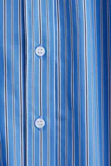 Camisa celeste y blanca a rayas verticales, de corte amplio y mangas largas con puños abotonados. Cuello clásico y cierre frontal con botones.
