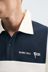 Polo de manga larga con corte relaxed fit, confeccionado en tejido con algodón. Presenta un diseño color block en azul marino, blanco y verde, con cuello solapa con cierre frontal de botonadura. Cuenta con bordados y parches combinados a contraste en delantero y espalda, y acabados en rib.