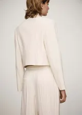 Chaqueta corta color crema con rayas verticales finas, cuello camisero, cierre frontal con botones ocultos, manga larga y dos bolsillos de parche en la parte delantera.