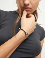 Pulsera rígida de aleación de metales bañada en plata de ley, con cuero marrón y cristal facetado verde en forma de lágrima.