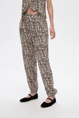 Pantalón slouchy de viscosa con estampado floral en tonos beige y negro, bolsillos laterales, cintura alta y detalle de punto smock en los tobillos.