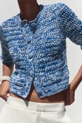 Chaqueta de punto azul y blanco con cuello redondo y manga francesa. Tiene bolsillos delanteros de plastrón y cierre frontal con botones a tono.