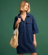 Vestido corto de jean azul con cuello camisero, escote en V, mangas cortas, dos bolsillos delanteros y corte recto.