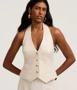 Chaleco color crudo confeccionado en viscolino, con escote halter, cierre frontal con botones, bolsillos delanteros falsos y bajo en V.