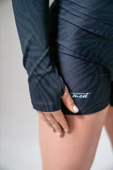 Remera deportiva de lycra negra con estampado de cebra, corte crop top, mangas largas con orificio para el pulgar y logo estampado en blanco.