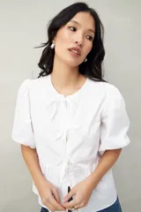 Blusa blanca de algodón con mangas abullonadas, escote redondo y lazos frontales.