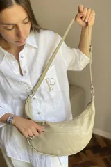 Cartera tipo bandolera de cuero sintético color celeste, con forma de media luna y tachas metálicas redondas plateadas en el frente. Posee correa ajustable y placa metálica con logo en la parte superior.