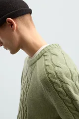 Sweater verde claro de punto con cuello redondo y mangas largas. Presenta diseño de trenzas en el centro y en las mangas.
