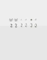 Set de seis pares de aros plateados, incluye aros tipo argolla, aros con forma de mariposa y aros con perlas.