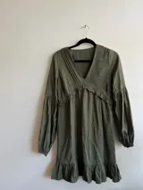 Vestido verde militar con escote en V, mangas largas y detalle de volado en la parte inferior.