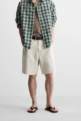 Bermuda color verde militar, de corte relaxed fit, con bolsillos frontales y traseros tipo plaqué, detalle de tira y bolsillo multifunción en la pierna, y bajo irregular.