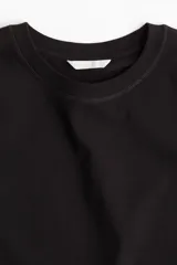 Remera negra de algodón, corte amplio, con cuello redondo y mangas cortas.