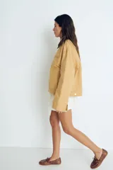 Campera color beige de algodón Oxford con cuello de pana marrón en contraste. Modelo de corte holgado con cierre frontal, hombros caídos, bolsillos laterales ribeteados y bolsillo superior con cierre. Ajuste con botones a presión en los puños y en la parte posterior del bajo.