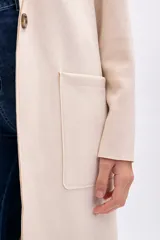 Blazer largo de mujer, color beige claro, con solapas amplias, bolsillos frontales grandes y corte recto.
