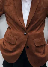 Chaqueta marrón de piel caprina con cuello de pico con solapa, diseño recto, cierre delantero con botones, forro interior, manga larga y dos bolsillos de solapa en la parte frontal.