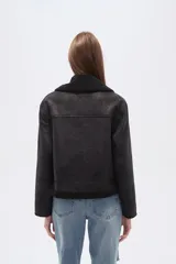 Campera negra de estilo aviador, confeccionada en material tipo gamuza o suede, con cuello y forro de corderito (shearling) negro. Presenta cierre frontal metálico y puños y ruedo con terminación de corderito.