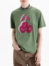 Remera verde de algodón pima, de mangas cortas, cuello redondo y fit amplio. Presenta una estampa frontal de tres cerezas en tonos rojos y blancos.
