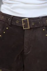 Short de gamuza color marrón oscuro, con tiro alto, cinturón incorporado con hebilla metálica y tachas doradas decorativas en los bordes de los bolsillos y el ruedo.