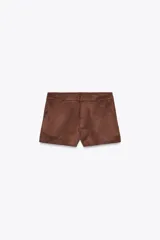 Shorts color marrón de tiro alto con bolsillos delanteros y cierre frontal con cremallera y ganchos metálicos.