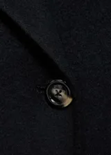 Abrigo largo negro de doble botonadura con cuello de solapa con muesca y hombros caídos.