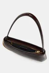 Bolso de hombro alargado color marrón oscuro, con asa corta y detalle metálico dorado en un lateral. Incluye bolsillo interior con cremallera y cierre principal con cremallera.