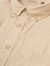 Camisa de hombre color verde oliva, de manga corta y corte clásico. Confeccionada en lino y poliéster, con cuello abotonado y bolsillo en el pecho.