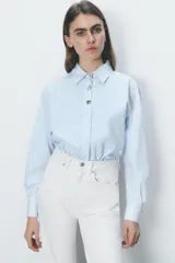 Camisa celeste a rayas verticales, de popelín, con cuello solapa, manga larga y cierre frontal con botones dorados.