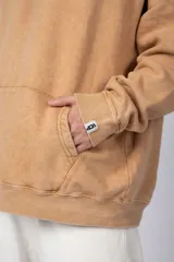 Buzo canguro color ocre con capucha y cordones negros, de corte oversize y confeccionado en tela de algodón friza con teñido artesanal y estampa circular en el pecho.