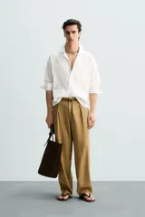 Camisa blanca de corte relajado confeccionada en tejido de algodón y lino. Tiene cuello bowling, manga larga con puños abotonados, jaretas en el delantero, bolsillos de parche en pecho y cadera, bajo con aberturas laterales y cierre frontal con botones.