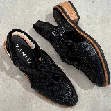 Zapato tipo sueco de cuero vacuno negro con textura reptil, con cordones y talón descubierto. Tiene suela de madera con altura de 4,5 cm en el talón y 1,5 cm en la parte delantera.