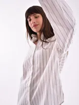 Camisa blanca con rayas verticales negras, de corte holgado, manga larga con puños abotonados y bolsillo en el pecho.