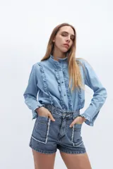 Camisa celeste de manga larga con cuello alto y volados en el frente y puños.
