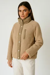 Campera color beige de corderito con cuello alto, cierre con botones a presión, manga larga y corte holgado.