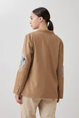 Blazer color tostado con bordados florales en azul y negro en la solapa y en la manga.