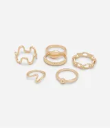 Set de seis anillos dorados de metal con diferentes diseños: uno con detalle de lunar, dos ondulados, uno de cadena, uno con lunar y uno irregular.