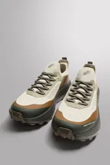 Zapatilla deportiva para hombre, color beige, con detalles en marrón y verde. Fabricada con tejido de punto transpirable y tecnología Shield Protect Max en puntera y talón. Cuenta con ajuste de cordones, tirador trasero, plantilla OrthoLite® extraíble, entresuela Spume Foam V3 y suela de goma.
