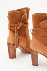 Botas de caña media de gamuza negra, con taco cuadrado y punta fina. Presenta tiras terminadas con borlas que se cruzan y atan alrededor de la caña.