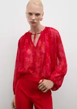 Blusa roja con estampado floral, de tejido fluido semitransparente y manga larga con puños elásticos. Tiene cuello redondo con cierre de lazo.